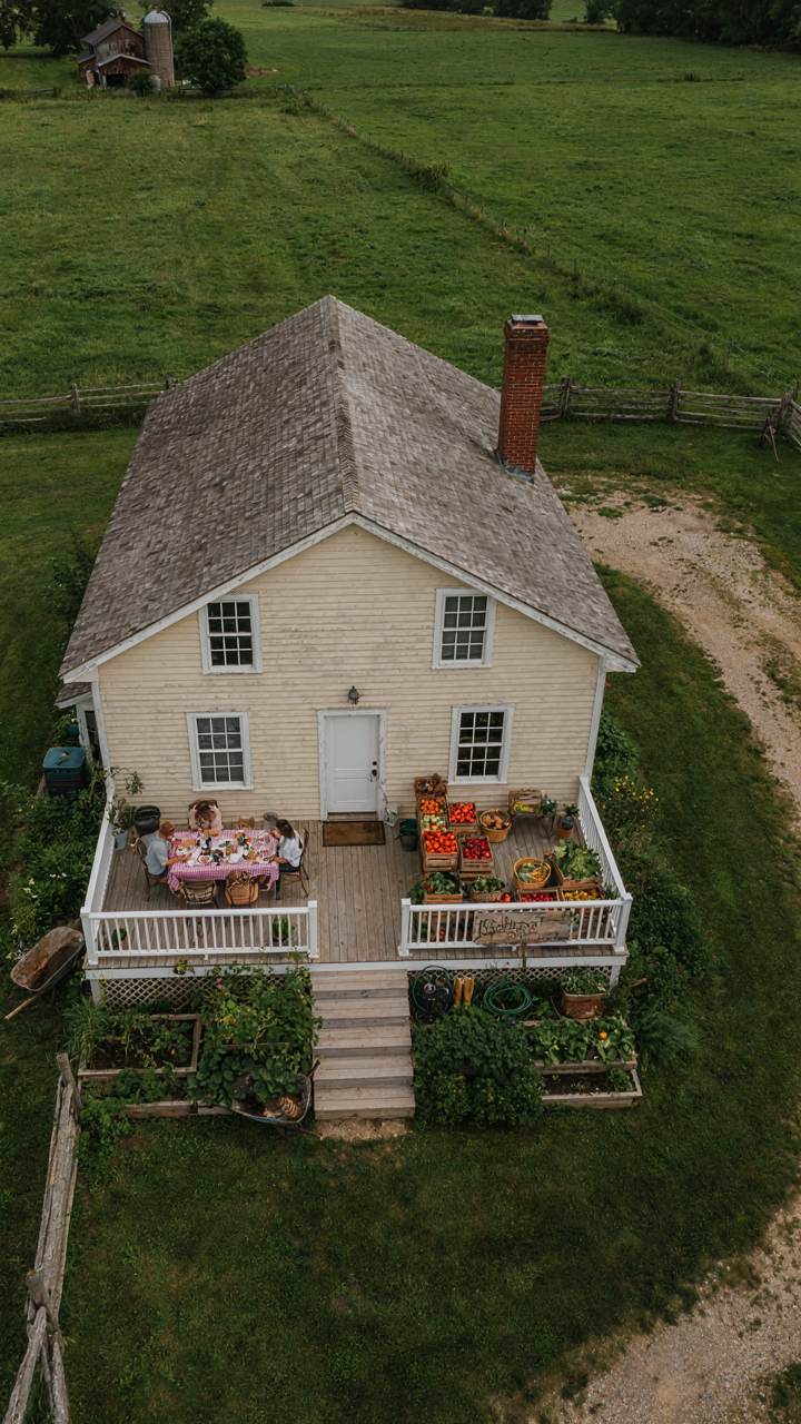 An aerial view shows a functioning farmhouse with a wraparound porch used for many activities.