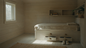 A tiny cabin bedroom with a built-in bed, integrated shelves, and warm sunlight.
