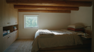 A cozy tiny cabin loft bedroom with minimalist built-in storage and a window overlooking a forest.