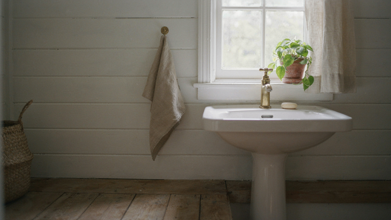 A sunlit tiny cottage bathroom with a white pedestal sink and a soft towel.