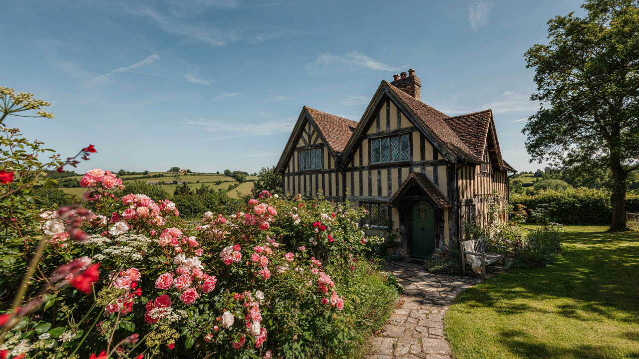 A picturesque Tudor cottage with steep gables and timber details under a blue sky.