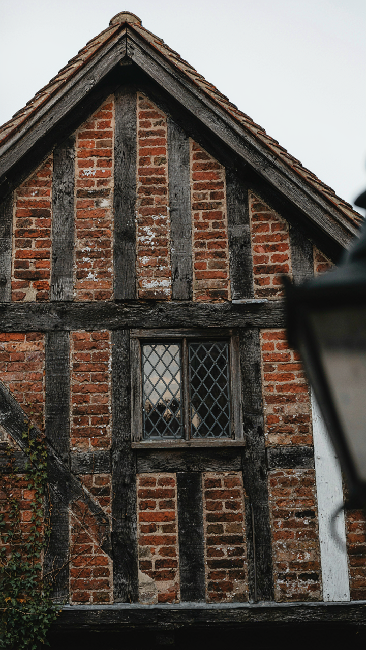 A weathered, asymmetrical facade of a tudor style house.