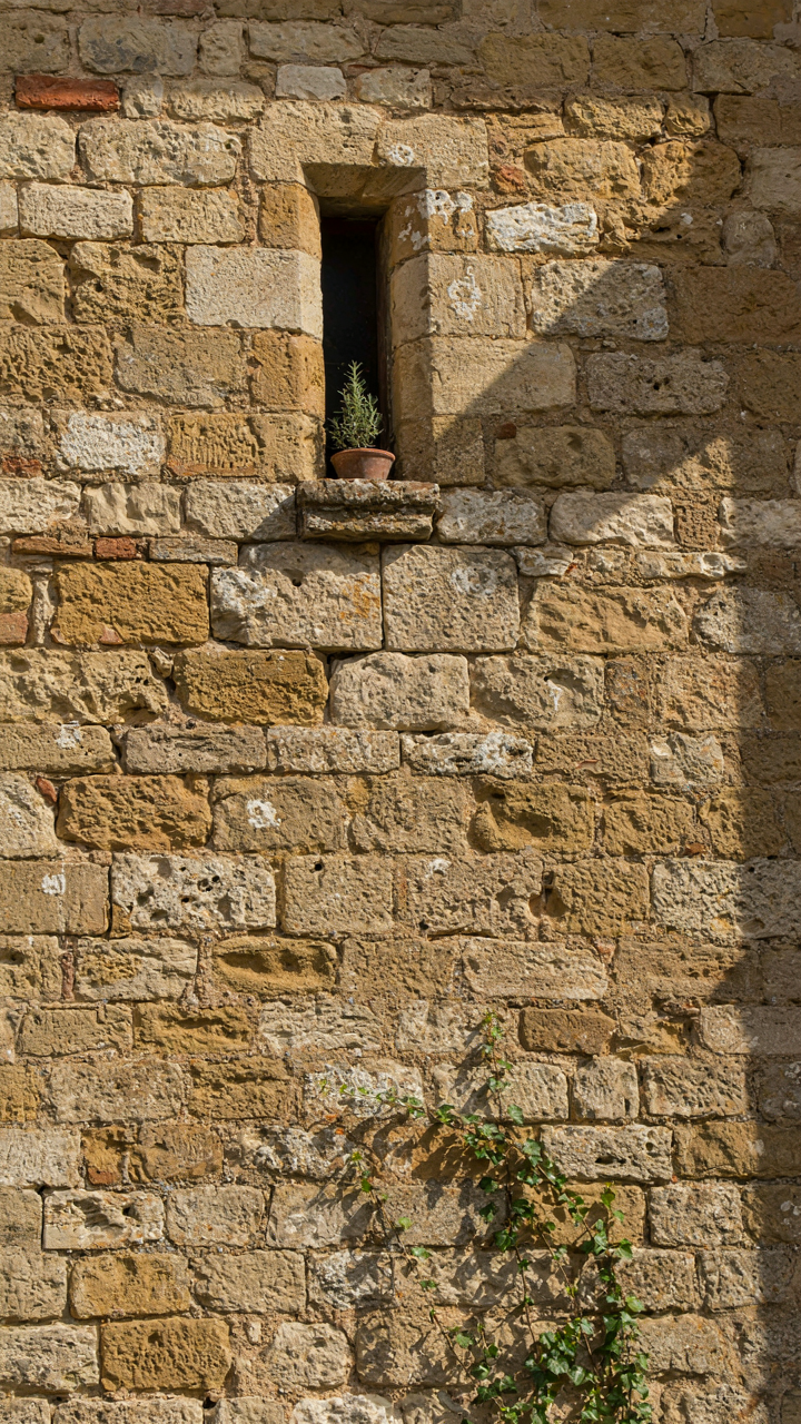 A very thick stone wall of a farmhouse with a small, deeply set window.
