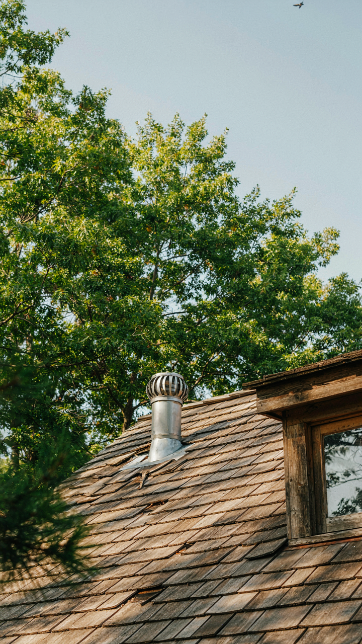 A small exhaust fan ducted through the sloped roof of a tiny cabin loft.