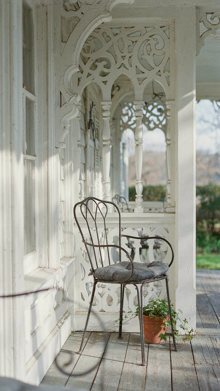 A simple wrought iron chair on a victorian porch with elaborate trim.