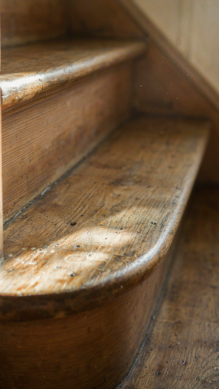A close-up of a well-worn wooden cottage staircase tread with deep indentations.