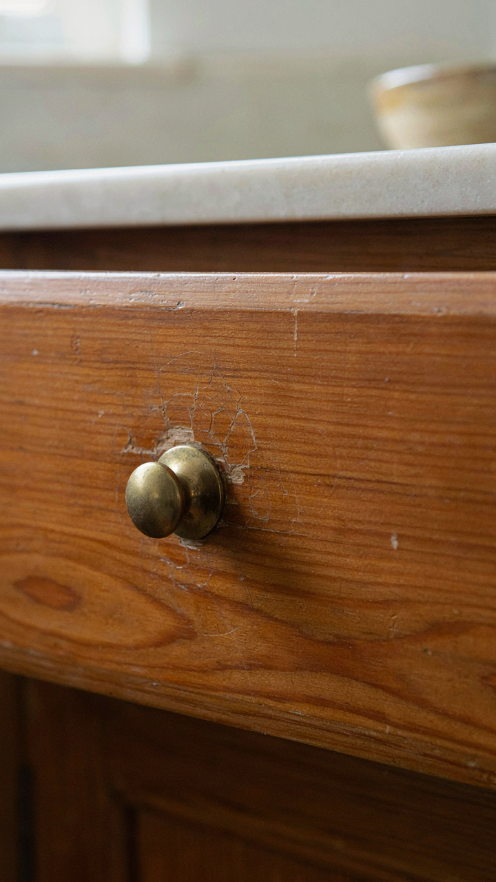 A wooden kitchen drawer shows authentic wear and cracked finish.