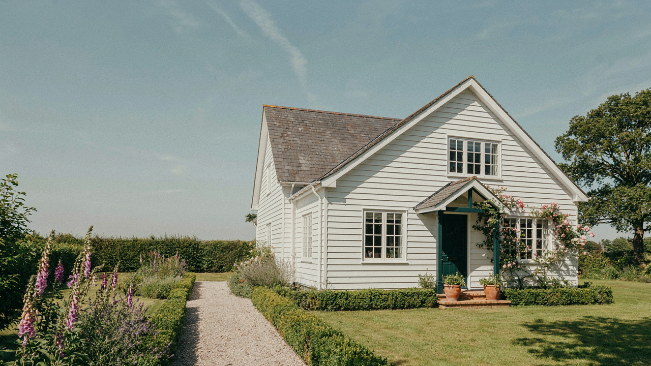 A charming white cottage exterior, bathed in bright sunlight, with a simple garden.