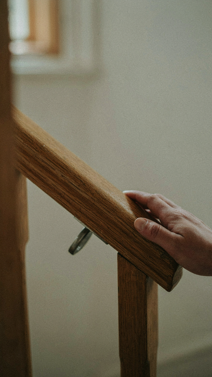 A hand gently touching a smooth, solid oak handrail.