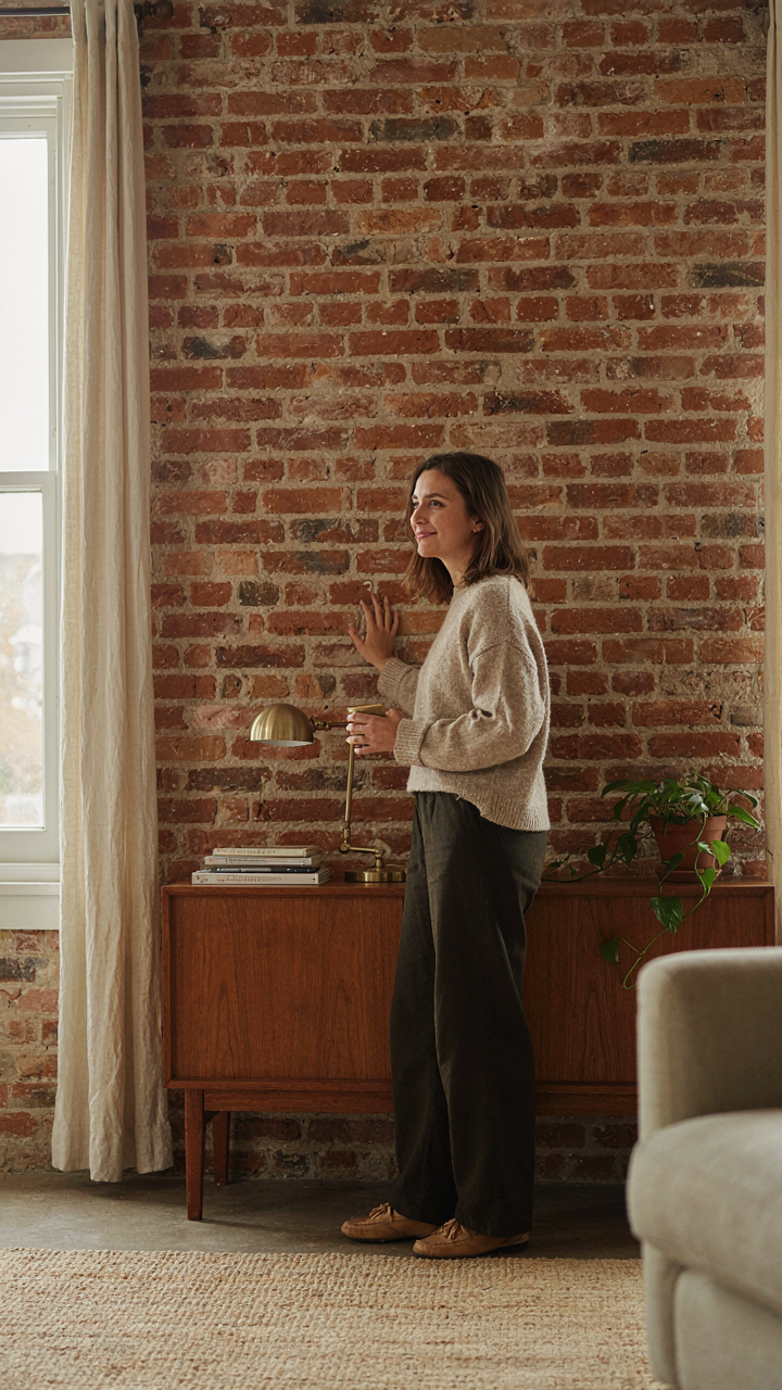 A person looks at an exposed brick wall in a bungalow, deep in thought.