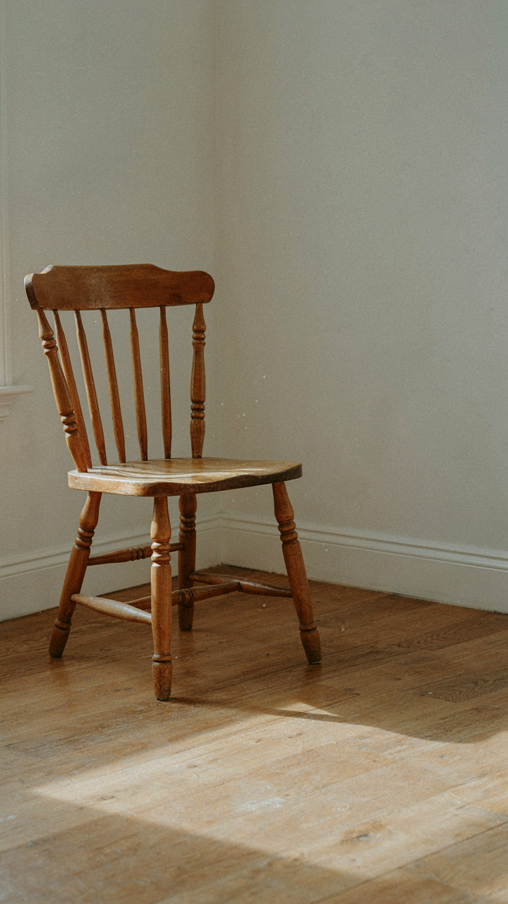 A single, aged wooden chair with hand-carved details in a sunlit room.