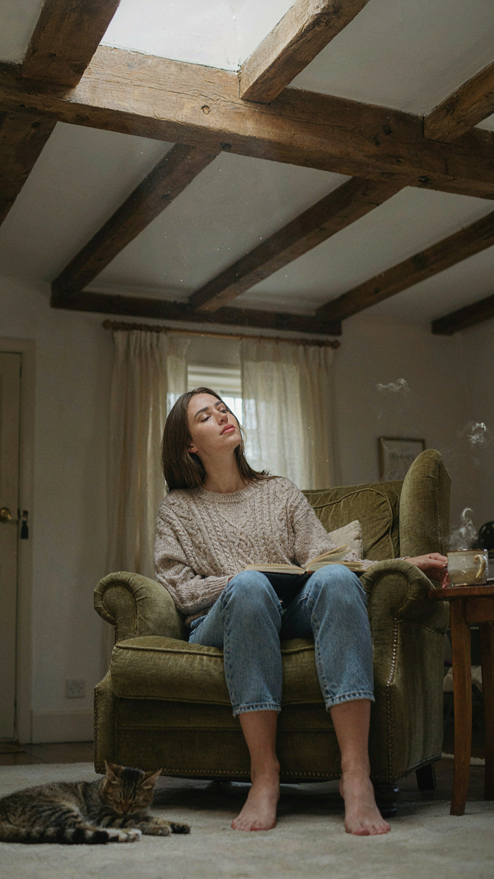A person relaxing in an armchair, gazing up at sturdy cottage ceiling beams.
