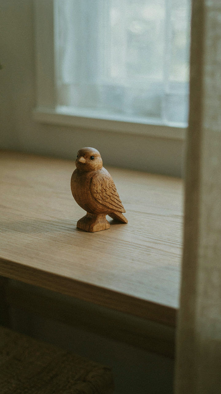 A carved wooden bird figurine sits on a clean desk in a she shed.